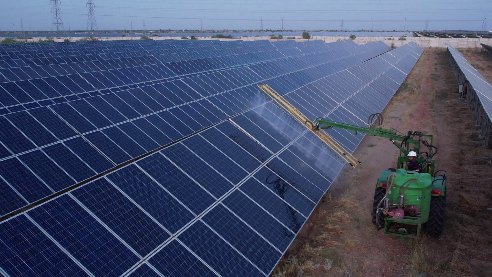 man on tractor using roller brush attachement to brush dust off rows of solar panels
