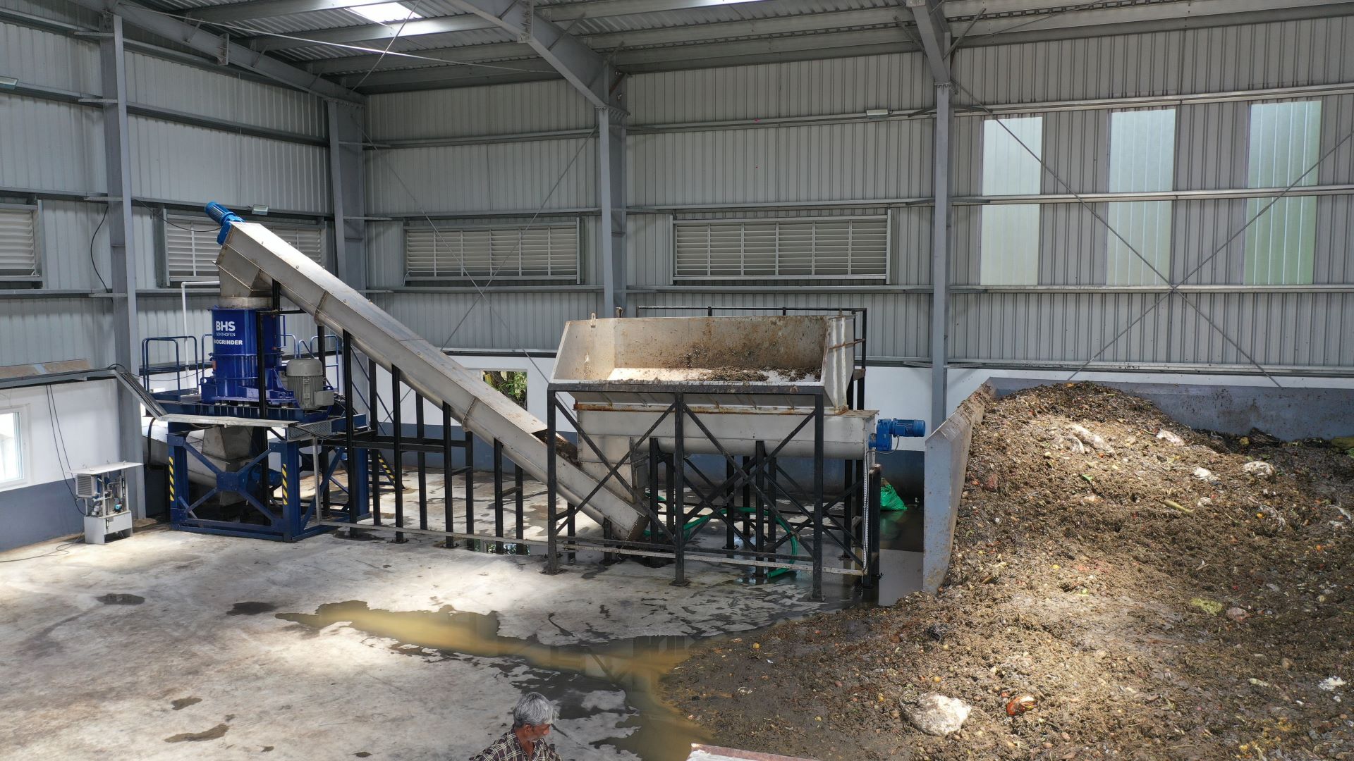 biomass material in a storage space next to metal process equipment all housed in a metal outbuilding