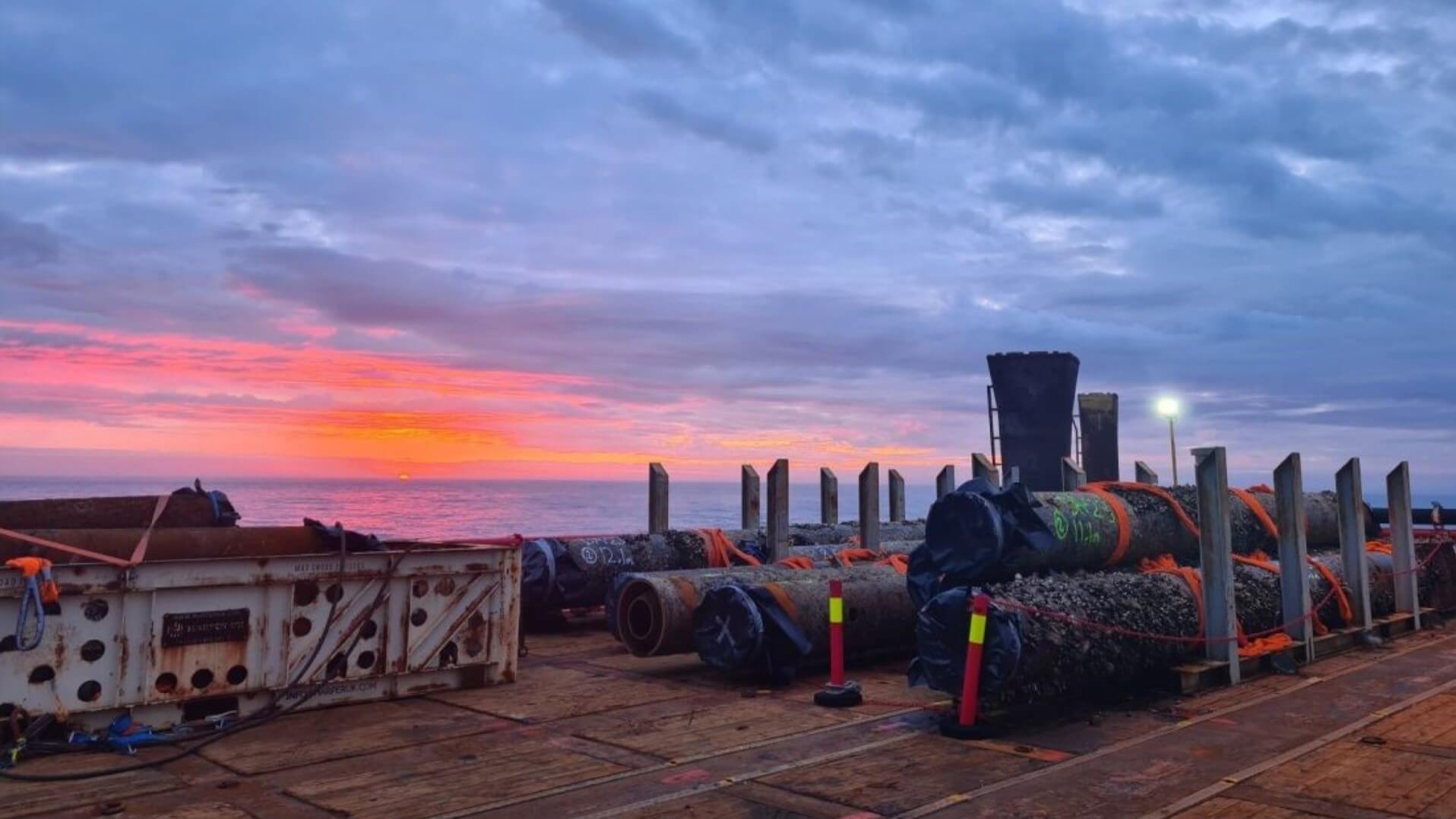 offshore pipework laying on side on deck of vessel at sea, against blue and pink sunset sky
