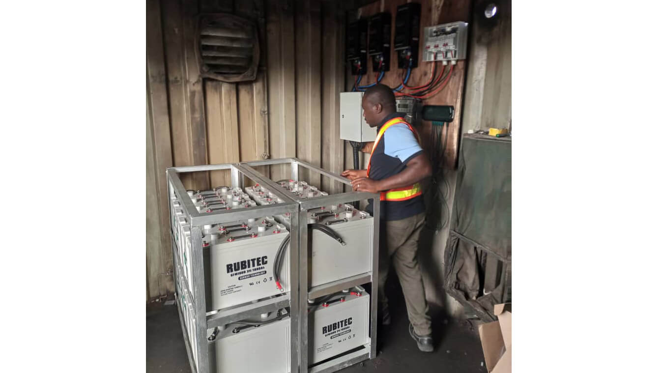 man standing next to stacks of lithium ion batteries in a dimly lit shet-like building