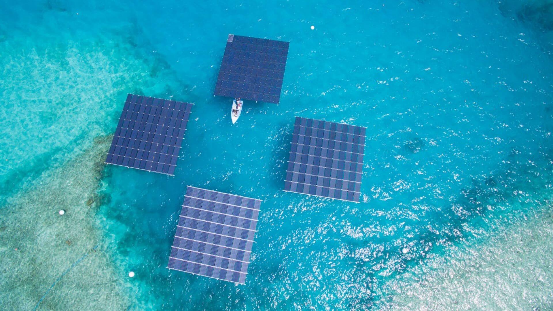 aerial overview of four groups of floating solar panels with a small boat in the centre of the grouping