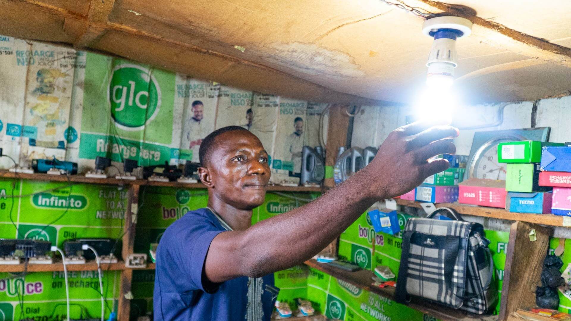 Nigerian man screwing in a lighted lightbulb to roof of storage room