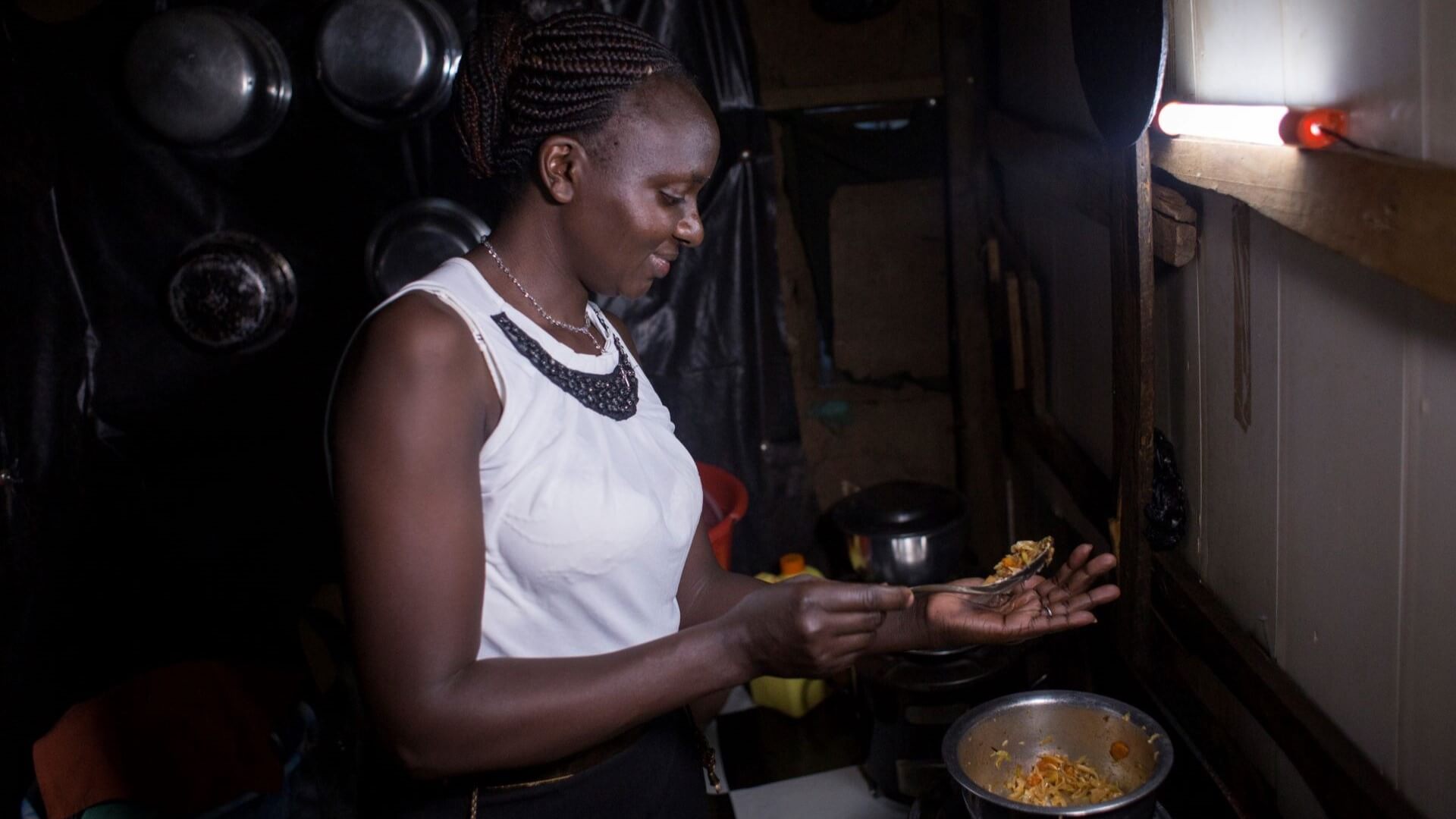 African woman cooking food on stove top in dimly lit kitchen