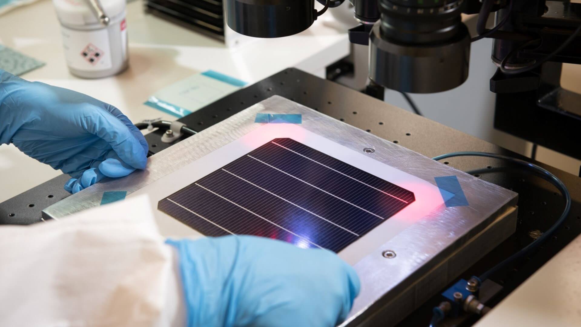 close up of solar cell being manufactured with lab technician's blue gloved hands in view