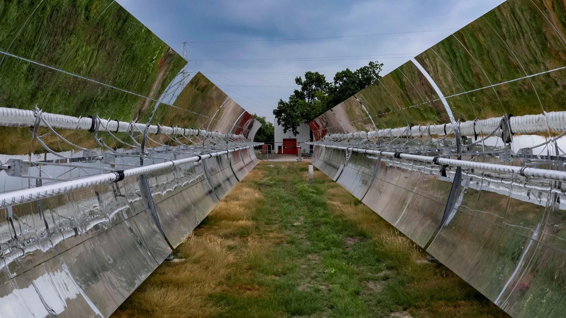 close up of row of parabolic mirrors at solar thermal installation with ground reflected in their surfaces