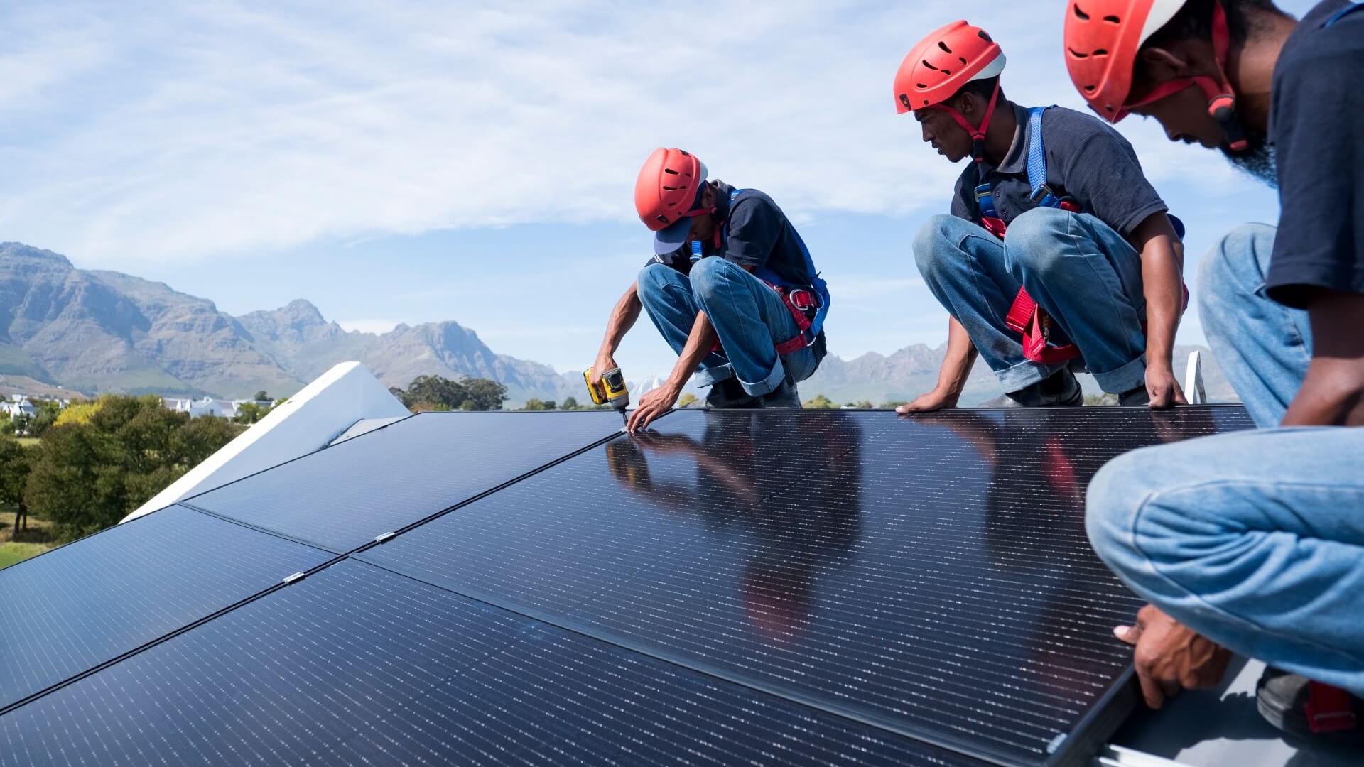 three engineers in hard hats installing rooftop solar panels