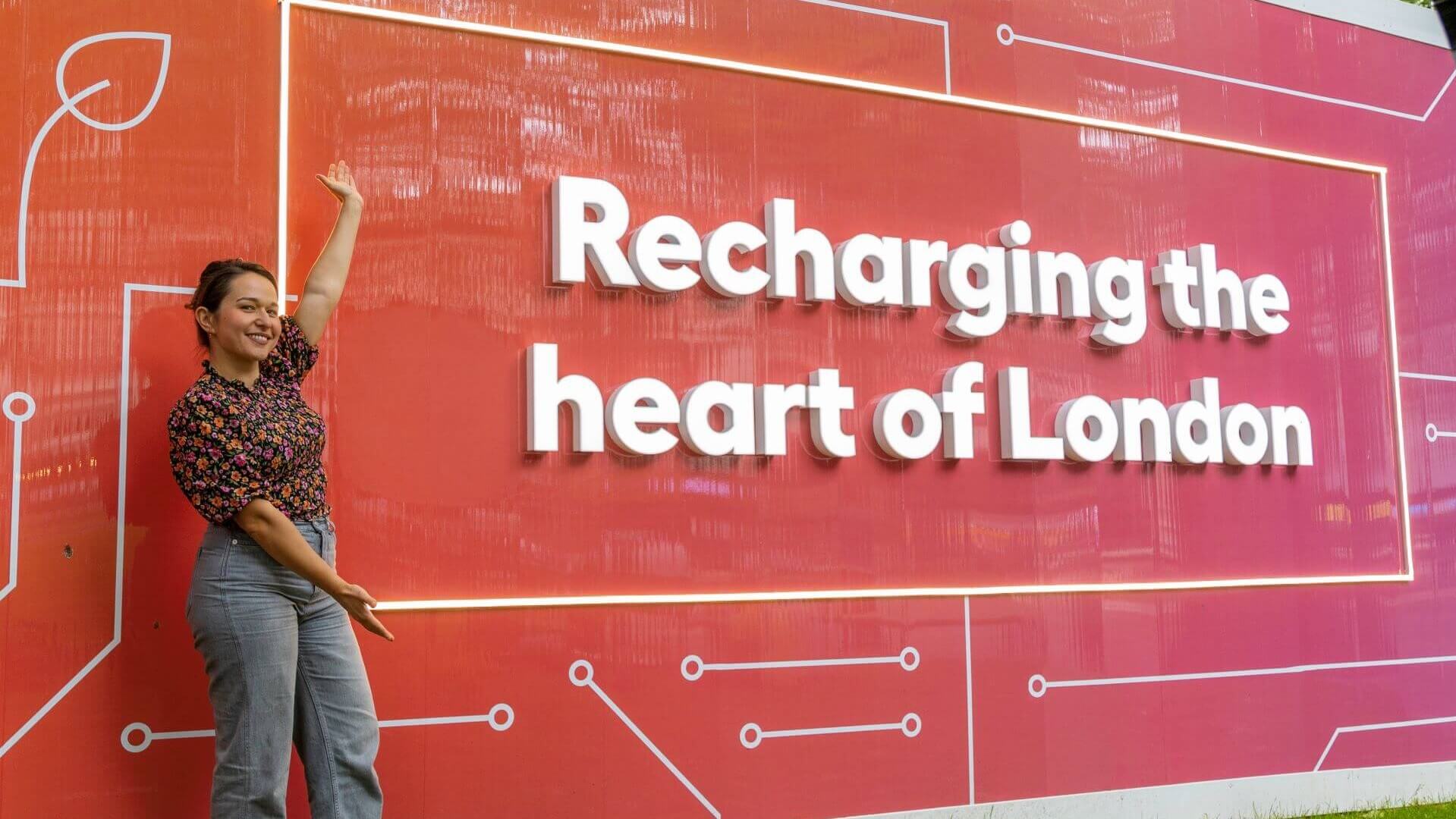 woman in front of red selfie board with stylised electricity circuit and company promo phrase Recharging the heart of London
