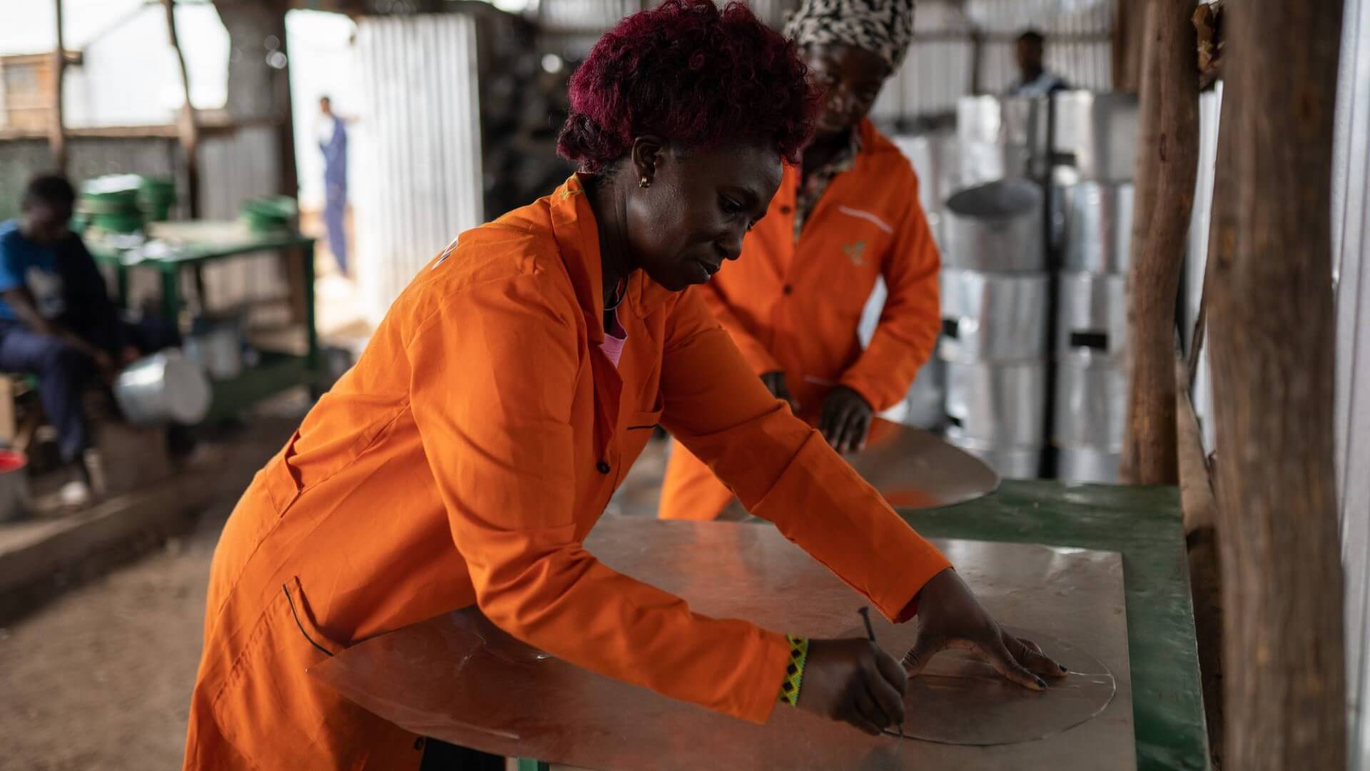 Kenyan woman in overalls in workshop drawing around a metal template on wooden board